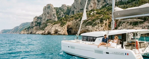 Catamaran blanc naviguant le long des falaises calcaires corses en Méditerranée